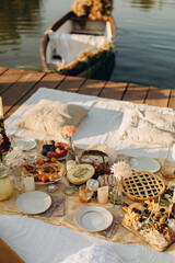 picnic on a wooden jetty near the water. a decorated picnic area awaiting guests. cheese and fruit plate on a picnic table. evening picnic party with golden sunlight.