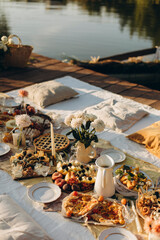 picnic on a wooden jetty near the water. a decorated picnic area awaiting guests. cheese and fruit plate on a picnic table. evening picnic party with golden sunlight. 