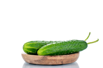 Two ripe green cucumbers on a wooden saucer, macro, isolated on a white background.