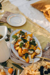 summer salad with fresh sliced peaches and mozzarella with basil leaves. sliced peaches and mozzarella on a large plate with a golden spoon. 