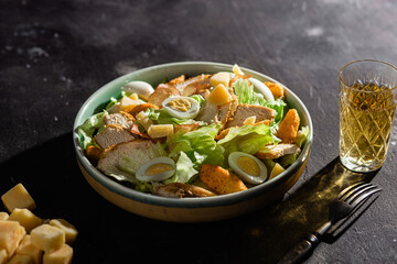 Caesar salad with chicken in a plate on a dark background