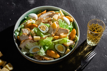 Caesar salad with chicken in a plate on a dark background