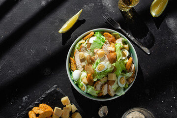 Caesar salad with chicken in a plate on a dark background
