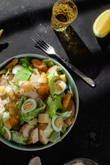 Caesar salad with chicken in a plate on a dark background