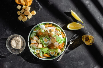 Caesar salad with chicken in a plate on a dark background