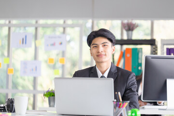Portrait of smiling young man sitting at his desk in the office, Businessman in suit working with laptop in office