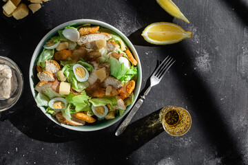 Caesar salad with chicken in a plate on a dark background