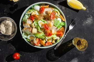 Caesar salad with chicken in a plate on a dark background