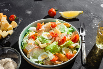Caesar salad with chicken in a plate on a dark background