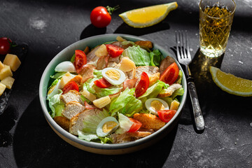 Caesar salad with chicken in a plate on a dark background
