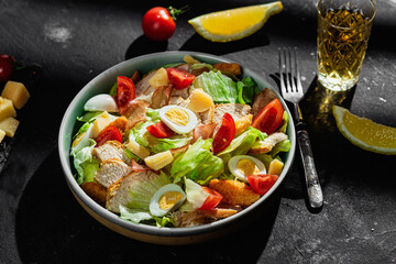 Caesar salad with chicken in a plate on a dark background