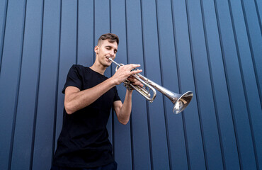 Young street musician playing the trumpet near the big blue wall