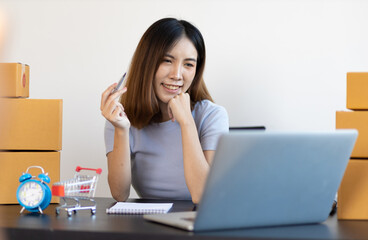 A young Asian woman starting a small e-commerce business is working on a laptop and chatting with customers over the internet.