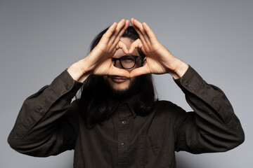 Portrait of young charming guy with long hair, gesturing heart sign with hands.