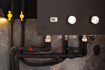 Close-up of plumbing connection to water gas heater of black colour.