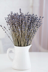 Provence. A beautiful bouquet of lavender in a white ceramic jug on the table. In the background is the interior of a modern white Scandinavian-style kitchen. The concept of home comfort.