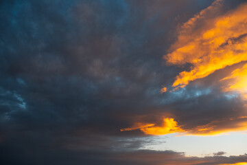 Fototapeta na wymiar Colourful sunlight of sunset falls on dark cloudy sky. Natural landscape.