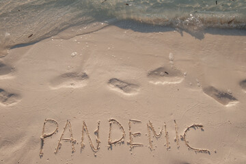 Pandemic. Handwritten text on smooth sand beach