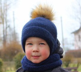 A little boy in winter clothes and a warm hat on the street.