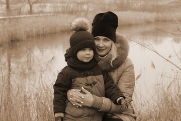 Mom and her little son are walking down the street in the countryside in winter. A little boy in a warm jacket and a winter hat