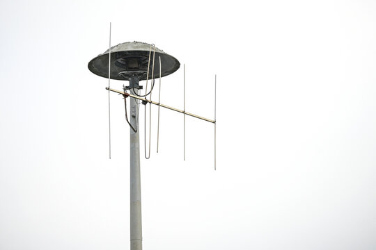 Pneumatic motor Siren, German E57, alarm for fire warning, natural disasters or attacks on a high pole that is also used for an antenna, light gray sky with copy space