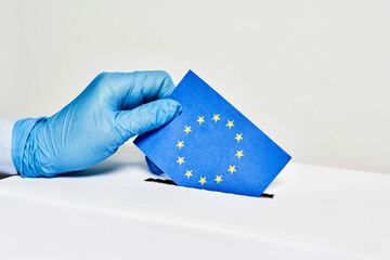 Hand holding flag of the European Union with ballot box during COVID-19 pandemic, concept of...