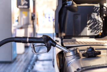 Truck refueling diesel at a highway gas station, close-up of the nozzle inserted in the vehicle's tank. - obrazy, fototapety, plakaty