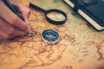 Hand use pen and marking and Magnetic compass, magnifying glass and diary on world map. Travel , Adventure and Discovery concept.