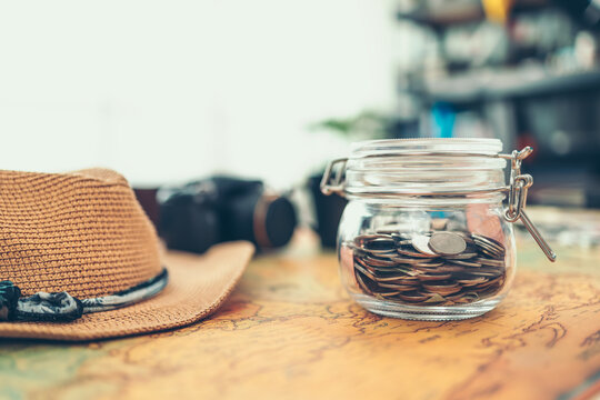 Travel money savings in a glass jar, camera, coffee cup, straw hat and pen on world map. Travel budget concept.