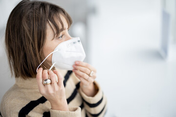 Young woman takes off face mask while getting ready for a lunch at modern restaurant, close-up. Wearing face mask at public spaces during pandemic concept