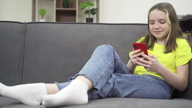 The little girl is smiling and looking at her smartphone while sitting on the couch. Entertaining content