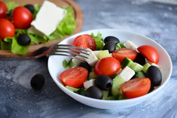vegetable salad with cherry tomatoes, black olives, cucumber and cheese in bowl with fork, close-up