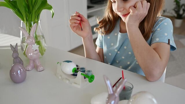 4K 60 fps of pretty little girl with pigtails painting easter egs at home