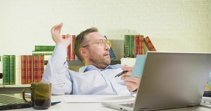 Middle-aged man is lounging in the office - he makes a paper airplane and flies it.