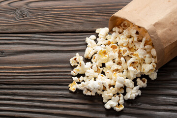Popped corn snack in paper bag on wooden table closeup