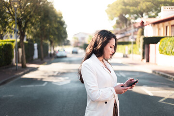 Fototapeta premium Young caucasian woman walking on the street using a smartphone.