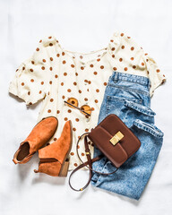 Set of women's summer clothes - blue mom jeans, polka dot blouse, chelsea boots  and  cross body bag on a light background, top view