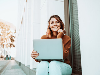 Happy amused young woman sitting watching in an urban street