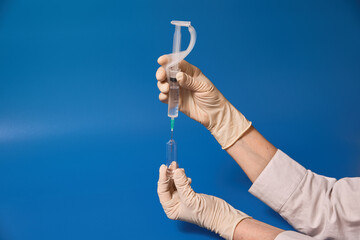 Gloved hand holding syringe on blue background 