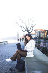 Young caucasian woman working with a laptop on a beach promenade.