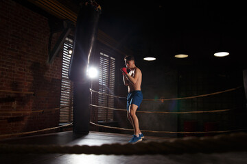 Fototapeta na wymiar A boxer trains in the gym strikes a punching bag.
