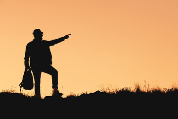 silhouette of man in hat on orange background with bag in his hand