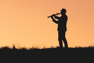 silhouette of a man playing the flute in a hat on an orange background