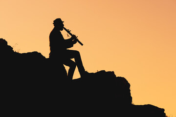 silhouette of a man in a hat sitting on a mountain and playing the flute