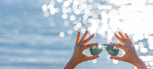 Sonnenbrille in einer Frauenhand vor unscharfen Hintergrund mit Bokeh Reflexen