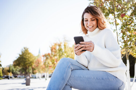 Young woman grinning to herself as she texts a phone message