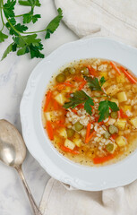 Pickle soup with pickled cucumbers, pearl barley, potatoes, onions, carrots and parsley. rassolnik in a white plate on a marble background. A traditional dish of Russian cuisine. Top view