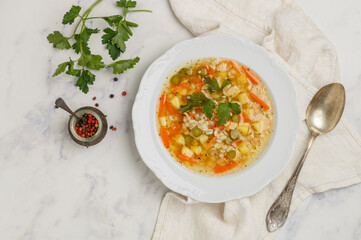 Pickle soup with pickled cucumbers, pearl barley, potatoes, onions, carrots and parsley. rassolnik in a white plate on a marble background. A traditional dish of Russian cuisine. Top view, Copy space