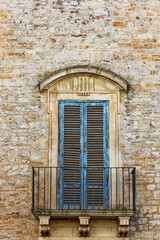 Ein blaues Fenster mit geschlossenen Fensterladen in einer Hausfront aus alten Steinen