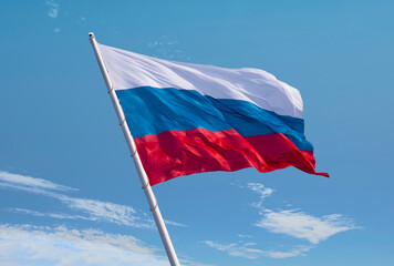 Russian flag waving in the wind over blue sky. The slope of the flagpole against gusts of wind. Small fragments of cirrus clouds.